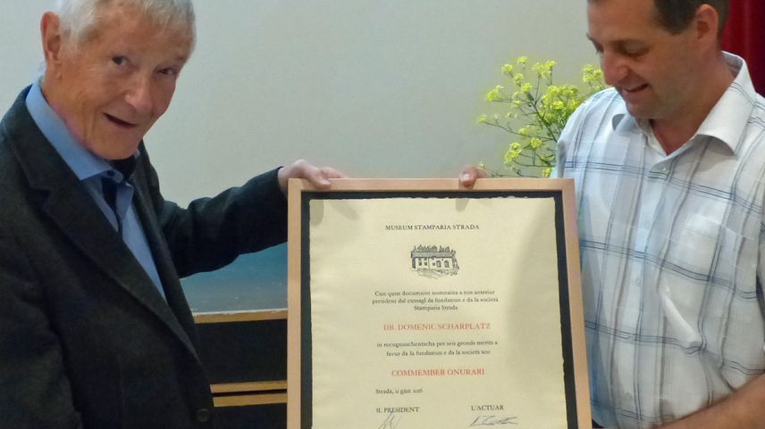 In recugnuschentscha per seis merits survain Domenic Scharplatz (a schnestra) da Georg Häfner il documaint sco commember d’onur da la Stamparia Strada (fotografia: Flurin Andry).