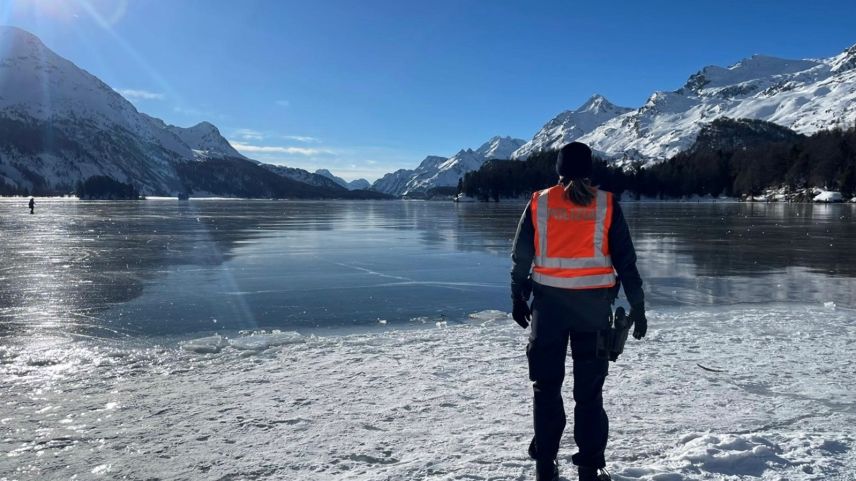 Eine Polizistin schaut auf den grösstenteils gefrorenen Silsersee. Im Hintergrund Berge und strahlendes Winterwetter (Foto: Kantonspolizei Graubünden).