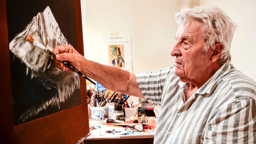 Hubert Bezzola, poliglot e cosmopolit, in seis atelier a Zernez cun ün purtret dal Piz Linard (fotografia: Jon Duschletta).