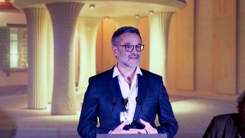 Giovanni Netzer, Gründer und Leiter von Origen, während seiner Ansprache. Im Hintergrund ein eingeblendetes Foto der neuen, modernen Bushaltestelle von Mulegns im Design des Weissen Turms, der Tor Alva. Fotos: Jon Duschletta