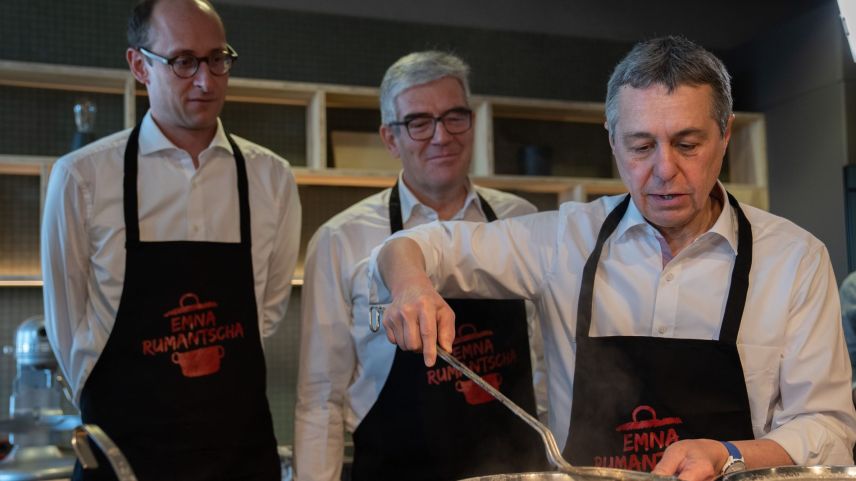 Cun sguard critic observan (da schnestra) Martin Candinas e Jon Domenic Parolini co cha Ignazio Cassis pes-cha ün bizoccal our da la padella (fotografia: mad).