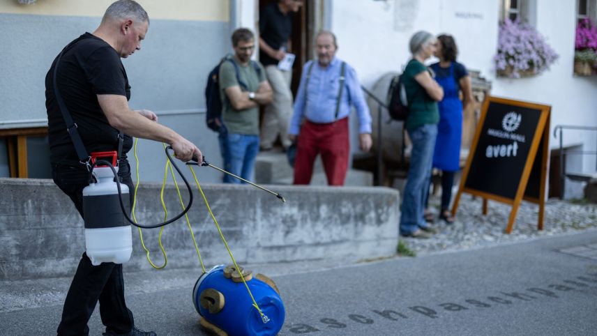 L’artist Pascal Lampert da Sta. Maria (a schnestra) ha performà davant il Muglin Mall sia inscripziun da «pasch» sülla via da Paclera (fotografia: Dominik Täuber). 