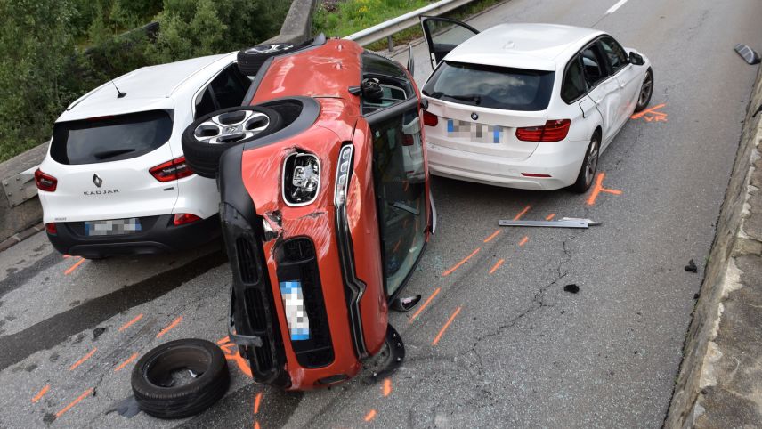 Zwischen zwei weissen Autos liegt das rote Auto der Italienerin auf der Seite (Foto: Kantonspolizei Graubünden).
