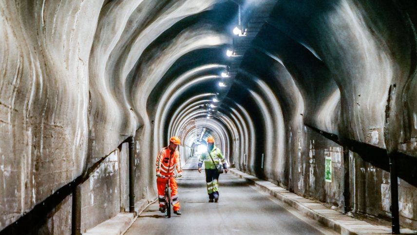 Bauarbeiter unterwegs im Tunnel Munt la Schera der Engadiner Kraftwerke AG. Gut zu erkennen sind die punktuellen Ausweitungen im Lichtraumprofil des Tunnels. 					Foto: Jon Duschletta
