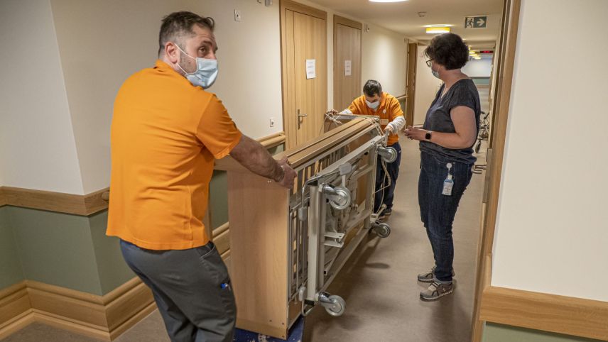 Die Leute des technischen Dienstes transportieren ein Bett vom Alt- in den Neubau. 