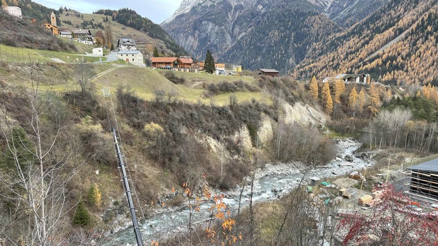 Auf dem Bild ist die Örtlichkeit zu sehen, wo der Mann gefunden werden konnte. Man sieht den Bach Brancla, Wiesland, Bäume, einige Häuser von Ramosch und die Bergwelt (Foto: Kantonspolizei Graubünden). 