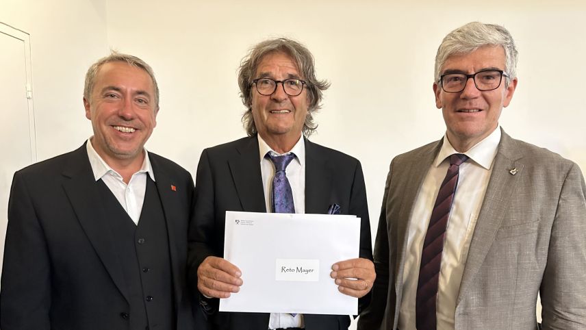 Il cusglier guvernativ Jon Domenic Parolini (a dretta) ha surdat il premi d'arcugnuschentscha dal chantun Grischun a Reto Mayer. A schnestra Andy Kollegger da l'Uniun da musica chantunala (fotografia: Nicolo Bass)