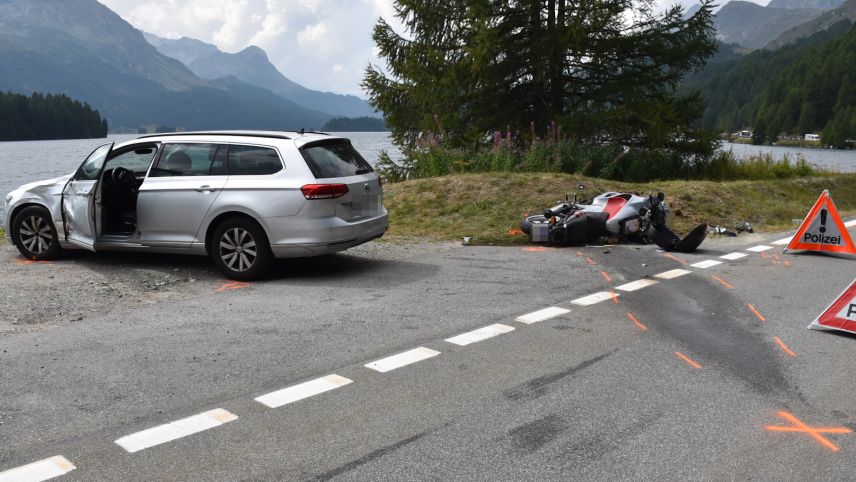 as Auto auf dem Ausstellplatz. Dahinter das am Boden liegende Motorrad. Im Hintergrund der Silser See (Foto: Kantonspolizei Graubünden).
