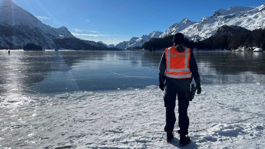 Eine Polizistin schaut auf den grösstenteils gefrorenen Silsersee. Im Hintergrund Berge und strahlendes Winterwetter (Foto: Kantonspolizei Graubünden).