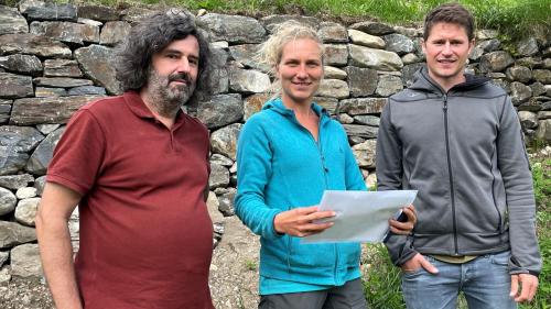 Johannes Florin, Lisa Zimmermann e Nicolas Ilg (da schnestra) davant il mür sech a Cha Noschas chi’d es gnü renovà (fotografia: Angelika Abderhalden).